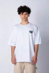 Remera blanca de corte oversize con mangas cortas y cuello redondo. Estampado pequeño en el frente con letras verdes.
