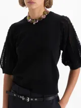 Top negro de largo a la primera cadera con mangas bombachas que incorporan flecos, aportando movimiento y textura al diseño. Confeccionado en una mezcla de hilados que combinan suavidad y estructura.