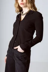 Camisa negra de tejido texturizado con cuello camisero, manga larga y cierre frontal con botones.
