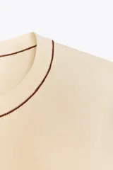 Top de punto color crema, de cuello redondo y manga corta con detalle de vivos a contraste en cuello y hombros.