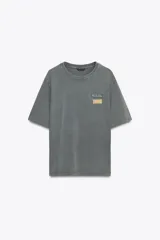 Camiseta gris de algodón con efecto lavado, cuello redondo, manga corta y parches estampados en el frente.