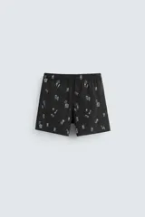 Bañador negro con estampado de dibujos en blanco. Tiene cintura elástica ajustable con cordón, bolsillos laterales y trasero.