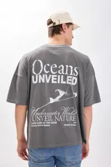 Camiseta manga corta gris oscuro con estampa de un paisaje marino y texto en color blanco. Corte amplio y recto, con proporciones cuadradas.