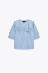 Camisa celeste a rayas verticales blancas, de corte recto, con cuello bobo con bordados y escote pico con lazada. Tiene mangas cortas abullonadas con elástico y cierre frontal con botones.