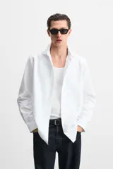 Camisa blanca de algodón, corte slim fit, cuello italiano, manga larga con puños abotonados y cierre frontal con botones.