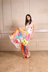 Vestido largo de seda con estampado vibrante y multicolor que incluye motivos frutales y caras sonrientes. Diseño de solera con escote halter anudado al cuello y falda amplia.