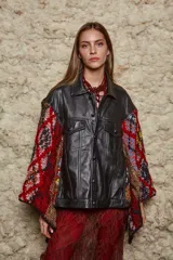 Chaqueta negra de cuero con corte clásico, cuello camisero, cierre frontal con botones y bolsillos con solapa en el pecho. Las mangas son tejidas en lana con diseño geométrico en tonos rojo, marrón, blanco y azul.
