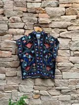 Chaleco negro con bordado floral multicolor, cuello mao y cierre frontal abierto.