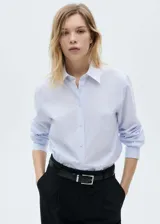 Camisa de popelina a rayas verticales celestes y blancas, de corte recto, con cuello camisero y mangas largas con puños abotonados.