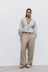 Blusa corta color celeste con textura arrugada, escote en V con puntilla, lazo ajustable en el frente y mangas 3/4 abullonadas con bordados florales a contraste.