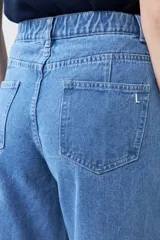 Pantalón de jean celeste de corte ancho, con cintura alta, pinzas y bolsillos laterales. Se ajusta a la cintura con un cinturón de cuero marrón.