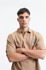 Remera polo color beige con textura acanalada, corte oversize, cuello clásico con botones y logo estampado en el pecho.