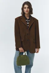 Chaqueta de gamuza marrón con diseño sastrero y corte levemente oversized. Presenta solapas de muesca, cierre frontal con botones y bolsillos laterales con solapa. Confeccionada en cuero vacuno con acabado tipo suede y forro de poliéster.