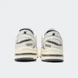 Championes New Balance modelo M1000, color crema con detalles en gris, confeccionados en cuero y malla, con logo "N" característico en los laterales y suela segmentada con amortiguación ABZORB.
