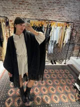 Ruana negra tejida a mano en lana merino con detalles de brillos y flecos.