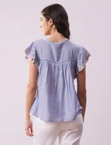 Blusa blanca de algodón con cuello a la base y escote en V con lazo de ajuste. Tiene mangas cortas con terminación amplia y bordados en delantera, mangas y espalda.