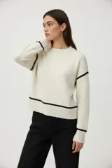 Sweater acrílico color blanco con rayas negras en los hombros, mangas y ruedo. Tiene cuello redondo y es de corte holgado.