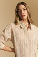 Camisa de manga larga color beige claro con bordado de flores blancas en relieve, cuello clásico y corte holgado.