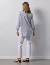 Blusa de gasa bambula a rayas verticales celestes y blancas, con cuello a la base, escote en V con botones y bordado floral negro. Mangas largas regulables con presilla y botón.