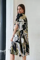 Vestido camisero midi con estampado de hojas en tonos negro, verde, gris y beige. Tiene cuello camisero, mangas cortas y cierre frontal con botones.