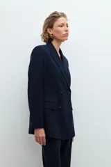 Conjunto de blazer, chaleco y pantalón de vestir de color gris con rayas verticales finas. El blazer es de doble botonadura, el chaleco tiene cuello en V y el pantalón es de corte palazzo.