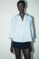 Camisa marrón de popelina con cuello solapa, escote en pico, cierre frontal con botones y mangas anchas con puños.