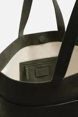 Bolso tipo shopper color verde musgo, confeccionado en cuero con acabado serraje. Tiene compartimento principal con cierre magnético, cuatro bolsillos exteriores y un bolsillo interior con cierre.
