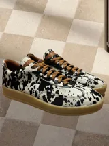 Zapatillas bajas con estampado animal print de vaca en blanco y negro, con cordones marrones y suela color caramelo.