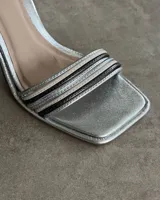 Sandalia de fiesta dorada con tiras finas cruzadas en el empeine, pulsera con hebilla al tobillo y taco geométrico.