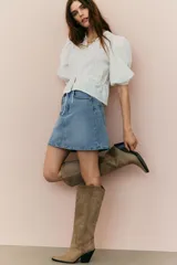 Blusa blanca de algodón con textura de lunares. Tiene escote redondo con lazo, botones en el frente, mangas tres cuartos abullonadas, cordón ajustable en la cintura y peplum.