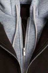 Campera negra de tejido suave efecto neopreno, con cuello y cierre frontal. Presenta un diseño de doble capa simulado con una capucha de tela gris claro que asoma por debajo del cuello de la campera.