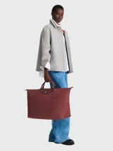 Bolso de viaje Longchamp modelo Le Pliage Green XL, color marrón ladrillo, confeccionado en lona de nylon reciclado con detalles en cuero ruso color marrón. Cuenta con doble asa de mano, cierre superior con cremallera y botón a presión, y es plegable para facilitar su almacenamiento.