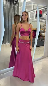 Conjunto de top y pollera larga color fucsia de satén. El top es de breteles finos y escote en V. La pollera es de corte recto y tiro alto.