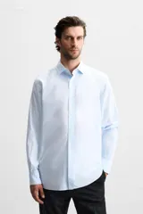 Camisa celeste a rayas verticales, de corte regular, confeccionada en algodón, con cuello italiano, manga larga con puños abotonados y cierre frontal con botones.