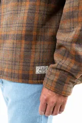 Camisa leñadora a cuadros marrón y naranja, forrada en corderito sintético, con cuello clásico, cierre frontal con botones, dos bolsillos frontales con tapa y puños abotonados.