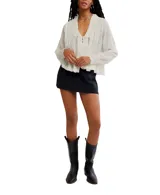 Blusa color crema de voile semitransparente con cuello y mangas largas con ribete de encaje, y botones en el frente.