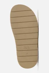 Zueco color beige de piel con acabado serraje, detalle trenzado en el empeine, plantilla acolchada y suela con volumen.