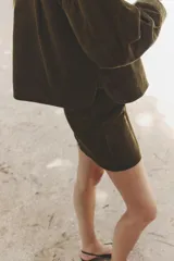 Pollera corta de corte evasé color verde oliva, confeccionada en pana con textura acanalada. Presenta cierre y botón frontal.