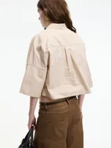 Camisa blanca cropped con botones en la parte delantera y mangas 3/4 con botones. Tiene pinza en la espalda.