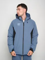 Campera corta de abrigo Umbro Crafted Pro, color negro con paneles laterales en gris. Presenta capucha con cordón ajustable, cierre frontal completo y logo de la marca bordado en el pecho.