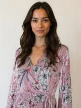 Vestido corto rosado con estampado floral, escote cruzado, mangas largas y lazo en la cintura.