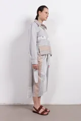 Camisa corta de algodón y seda con silueta recta, diseño a rayas verticales en tonos gris, blanco y beige, cuello camisero, cierre frontal con botones, mangas largas con puños abotonados, bolsillos de parche con botón a presión en el pecho y bajo recto.