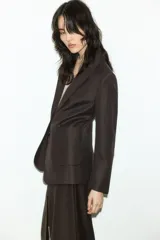 Blazer marrón de corte entallado, con solapas de pico, cierre de un botón, hombreras, bolsillos delanteros de parche, puños con abertura y botón, abertura trasera y forro interior.