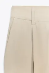Pantalón color beige de tiro medio con trabillas, pliegues frontales y corte ancho.