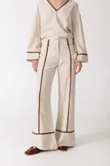 Pantalón de vestir color manteca con finas rayas verticales marrones, corte palazzo y detalles de ribete marrón en los laterales.