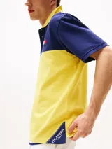 Chomba Tommy Hilfiger de corte amplio, con diseño color block en azul y amarillo, cuello clásico, cartera de tres botones, logo bordado en el pecho y logo oversize en la espalda.