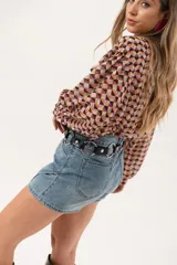 Minifalda de jean azul claro con corte evasé, detalle de short interno y cinturón negro con argollas metálicas.