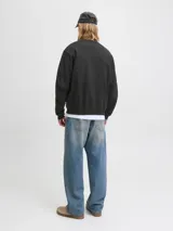 Buzo de manga larga y cuello redondo, color negro, con fit holgado. Presenta un estampado frontal en tonos verde menta y blanco con texto que incluye "Originals Studio", "Daily Basics", "International", "connecting CREATIVITY ACROSS DISTANCES" y "est. 90".