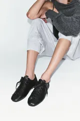 Zapatos tipo blucher de piel negra, con pespuntes decorativos, punta redonda y cierre de cordones. Suela de 1 cm de altura.