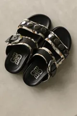 Sandalias bajas de cuero marrón con doble tira, hebilla ajustable y apliques de tachas metálicas.